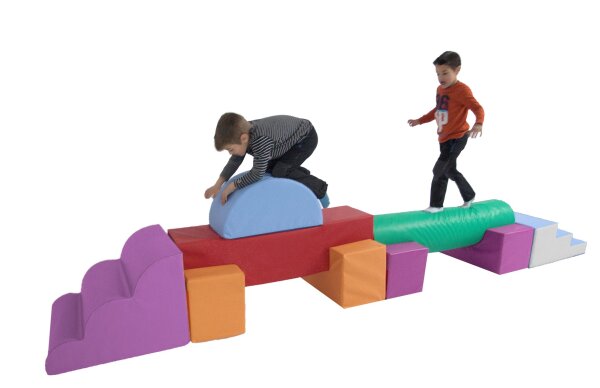 Zwei Kinder balancieren und klettern über einen langen Motorik-Parcours aus bunten Softbausteinen – fördert Gleichgewicht, Koordination und Bewegungsfreude.