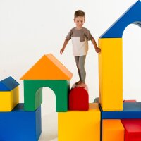 Kind steht auf bunten, großen Bauklötzen in verschiedenen Formen