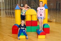 Drei Kinder spielen mit bunten Bauklötzen in einer Sporthalle