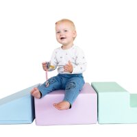 Kleines Kind sitzt auf bunten Schaumstoffblöcken und hält einen Beißring