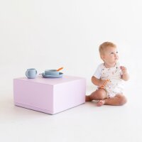 Kleinkind sitzt neben einem rosa Spieltisch mit Geschirr und Besteck
