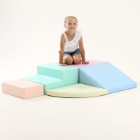 Kind sitzt auf bunten Schaumstoffbausteinen in verschiedenen Formen und Farben