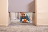 Lächelndes Kind krabbelt unter einem Möbelstück mit Spielzeug in der Hand