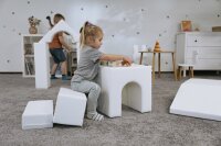 Kind spielt mit weißen Schaumstoffbausteinen in einem Spielzimmer