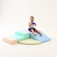 Kind sitzt auf bunten Schaumstoffbausteinen und spielt mit einem Spielzeug
